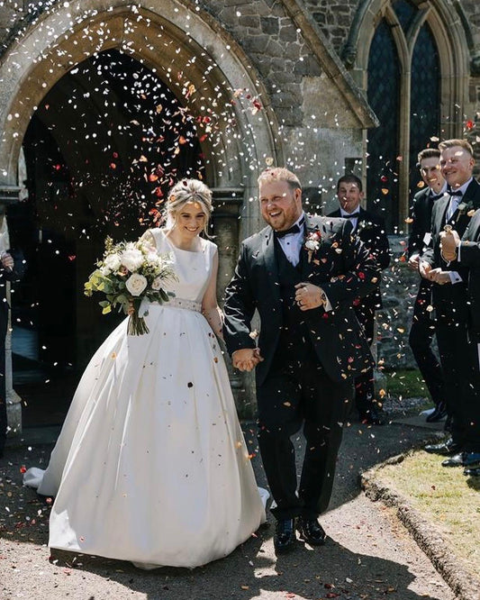 a bride and groom outside the church with confetti being thrown all over them, the bride wears bespoke hand-beaded belt and hand embroidered veil.